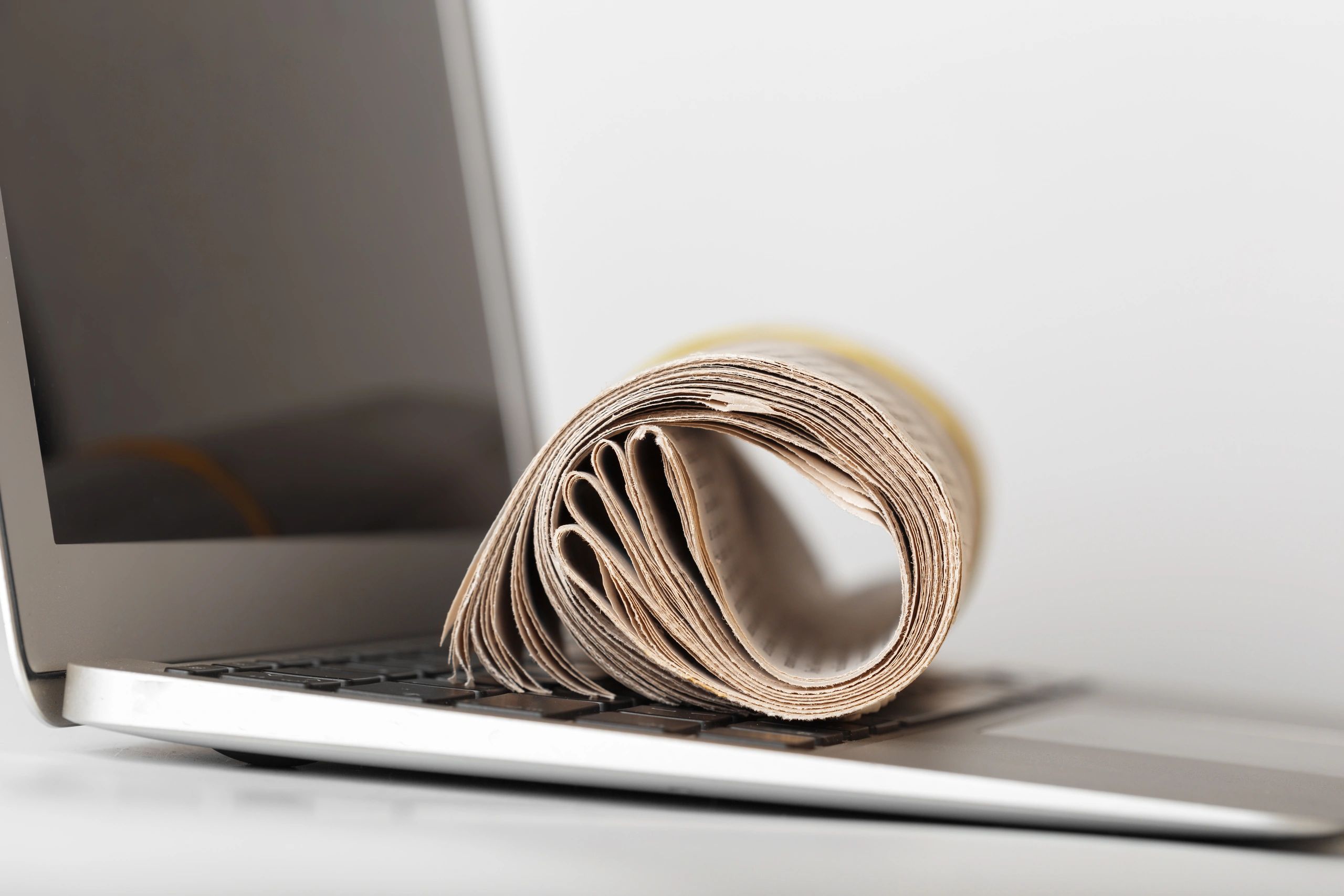 Rolled newspaper on a laptop keyboard in a workspace